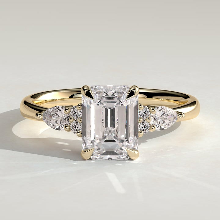 Emerald cut moissanite engagement ring with pear and round cluster shoulders in yellow gold