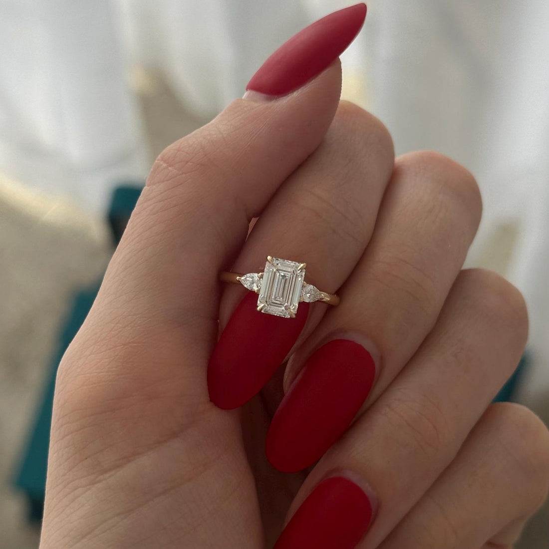 Emerald cut moissanite petite three stone engagement ring with pear side stones in yellow gold