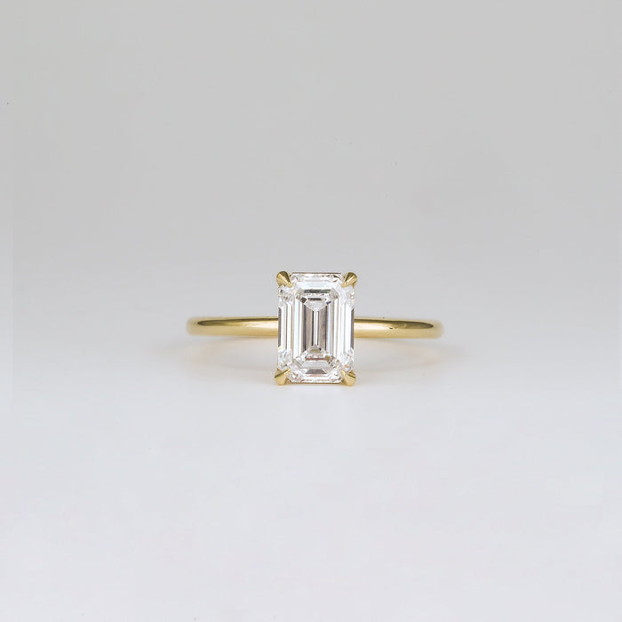 Emerald cut moissanite petite four claw solitaire engagement ring on a fine yellow gold band