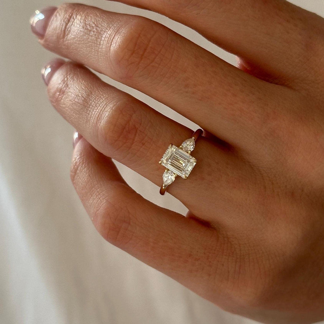 Emerald cut moissanite three stone engagement ring with pear side stones in yellow gold