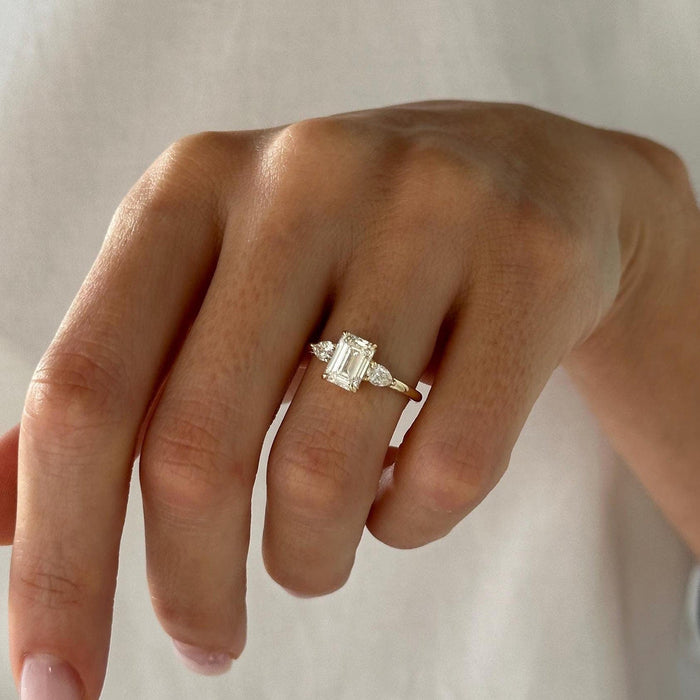 Emerald cut moissanite three stone engagement ring with pear side stones in yellow gold, view 2
