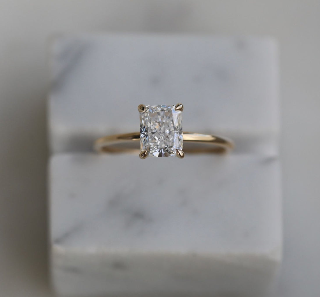 Elongated radiant cut moissanite solitaire engagement ring on a round wire yellow gold band