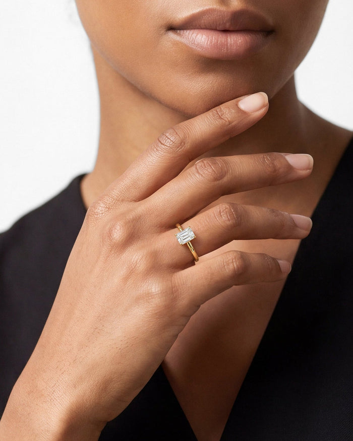 Emerald cut lab grown diamond solitaire ring in yellow gold worn on the hand at the chin