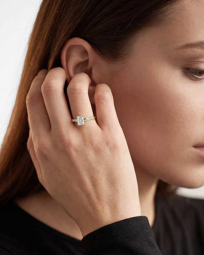 Emerald cut lab grown diamond infinity twist ring in yellow gold worn on a hand tucking hair behind the ear