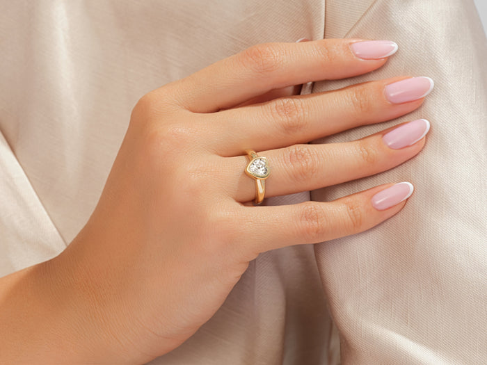Heart moissanite bezel engagement ring in yellow gold worn on the hand against beige silk