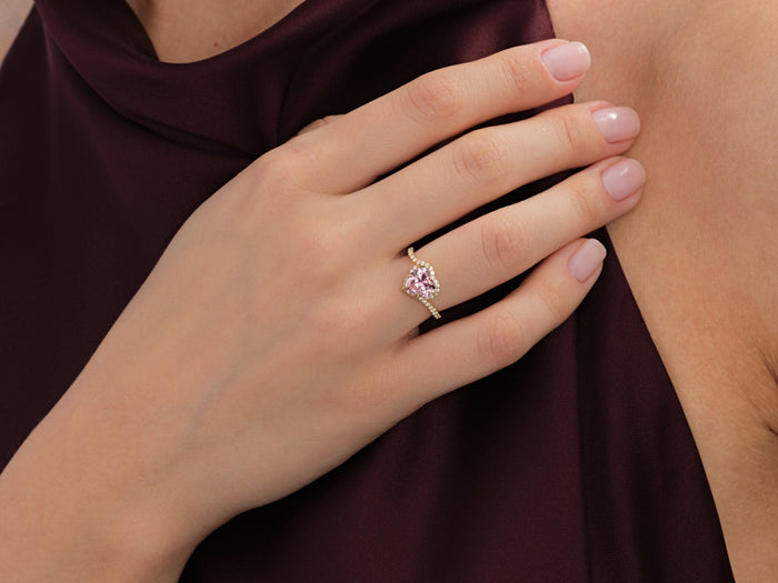 Heart halo bypass pave ring setting in yellow gold worn on the hand at the neckline, pink display stone