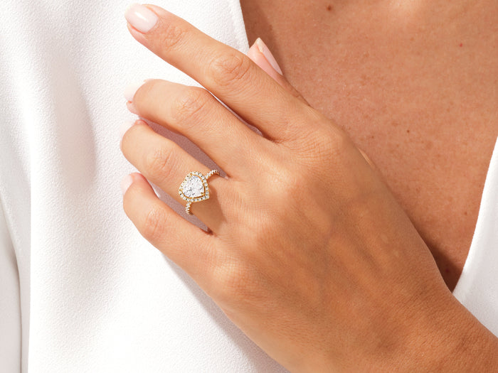Heart moissanite halo ring in yellow gold worn on the hand against a white shirt