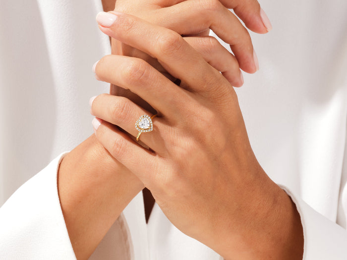 Heart cut moissanite halo ring in yellow gold on the hand, fingers interlaced