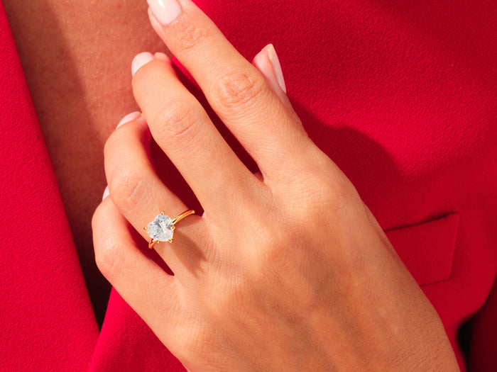 Large heart lab grown diamond knife edge statement ring in yellow gold on a hand against red fabric