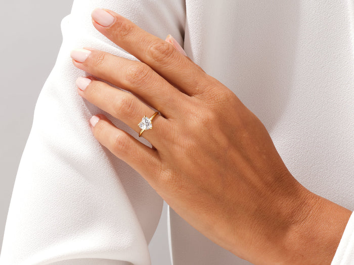 Heart shaped lab grown diamond five prong ring in yellow gold on a hand resting on a white sleeve