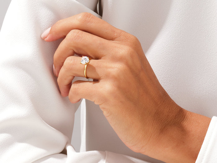 Heart cut moissanite solitaire ring in yellow gold worn on the hand with a white blouse
