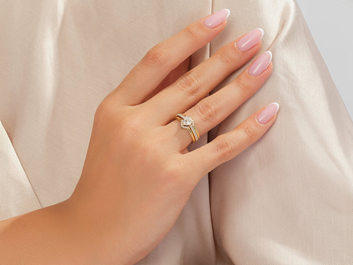 Heart lab grown diamond bridal set worn stacked on the ring finger against beige fabric
