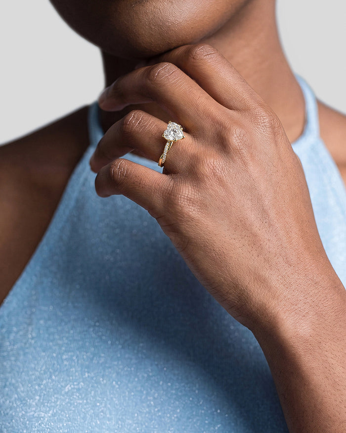 Heart shaped lab grown diamond twist ring in yellow gold on a hand at the chin with a blue top
