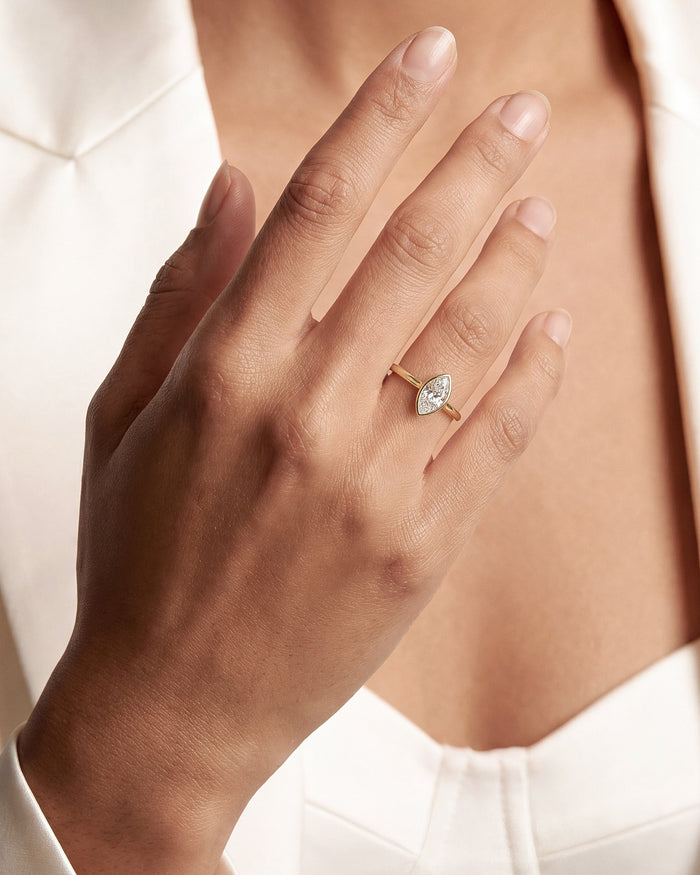 Marquise cut lab grown diamond full bezel ring in yellow gold on a hand against a white blazer