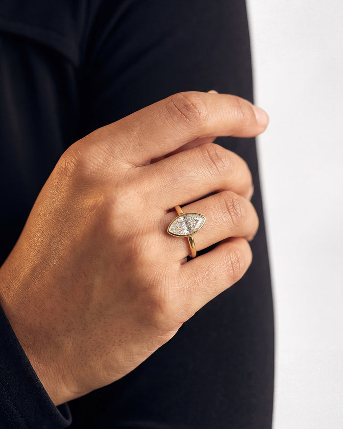 Marquise lab grown diamond bezel ring in yellow gold on a hand against a black sleeve