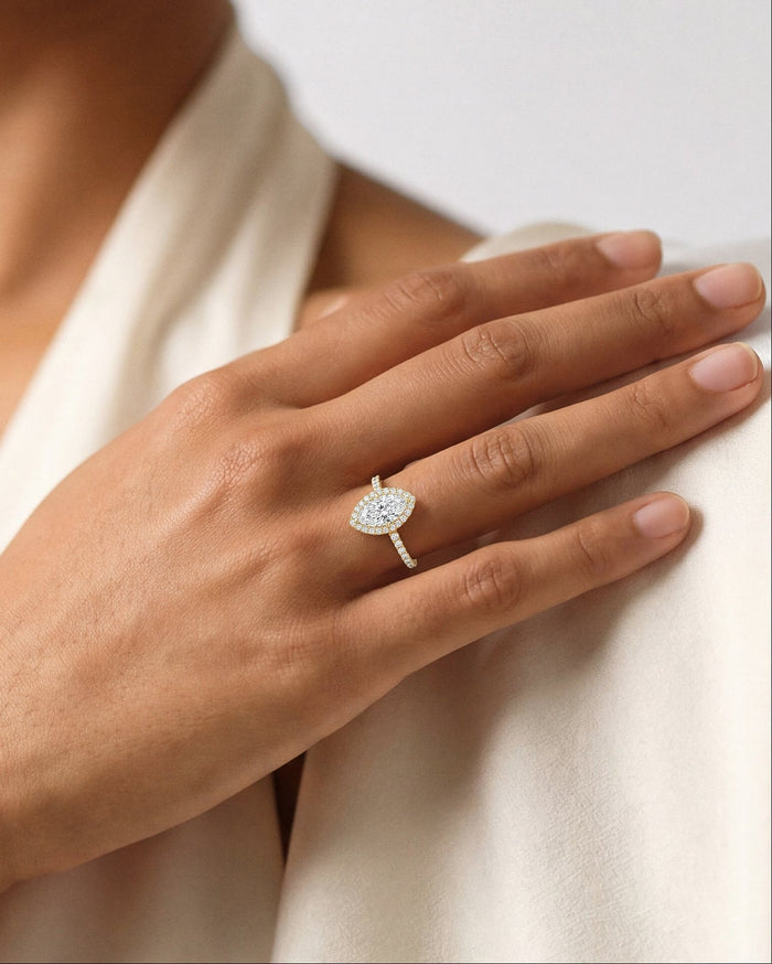 Marquise lab grown diamond halo ring worn on the hand resting on a cream top