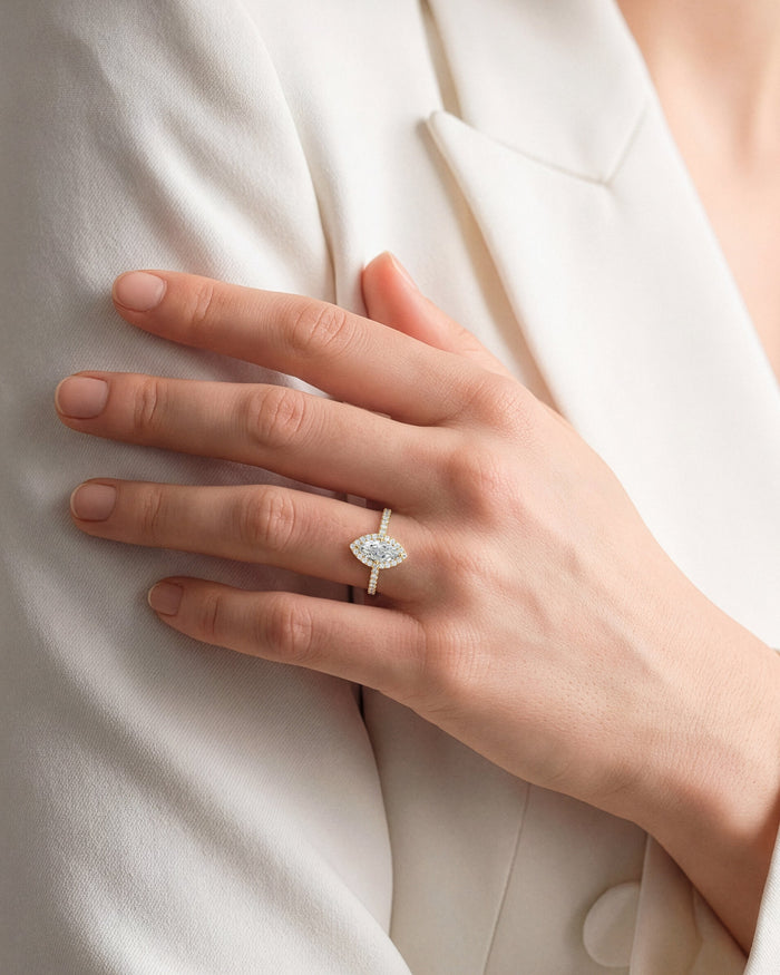 Marquise moissanite halo ring with pave band in yellow gold worn on the hand against a white jacket