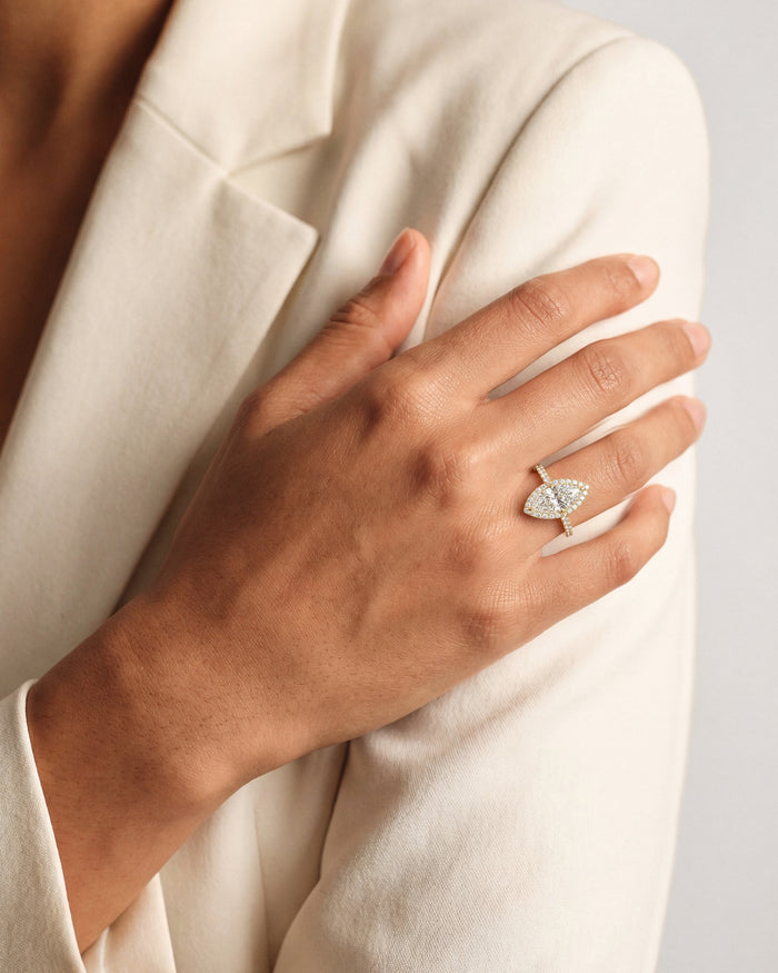 Marquise moissanite halo ring in yellow gold worn on the hand resting on a cream blazer