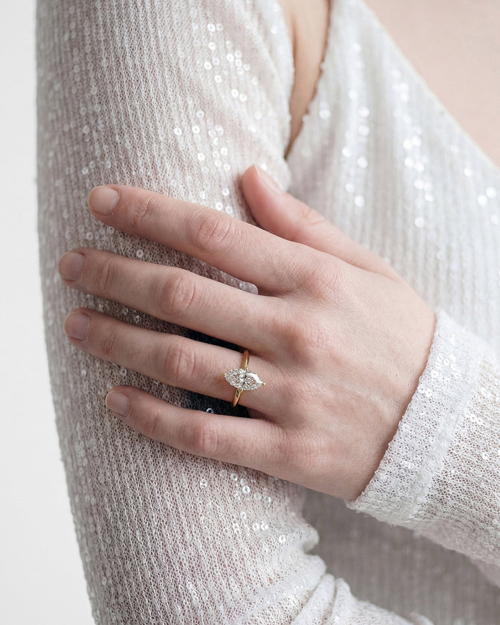 Marquise lab grown diamond knife edge solitaire ring in yellow gold worn on a hand resting on a sequin sleeve