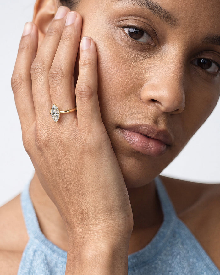 Marquise cut lab grown diamond knife edge ring in yellow gold on a hand held to the cheek