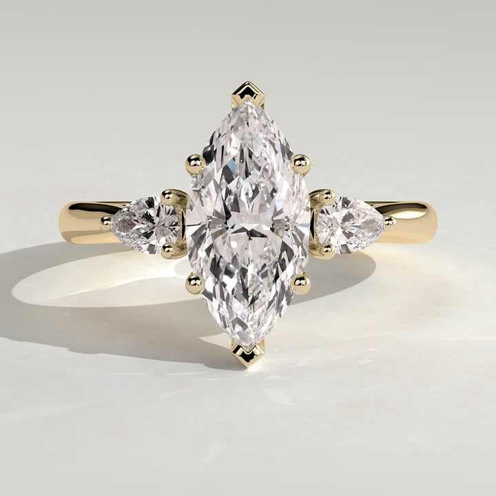Marquise moissanite three stone engagement ring with pear side stones on a fine yellow gold band