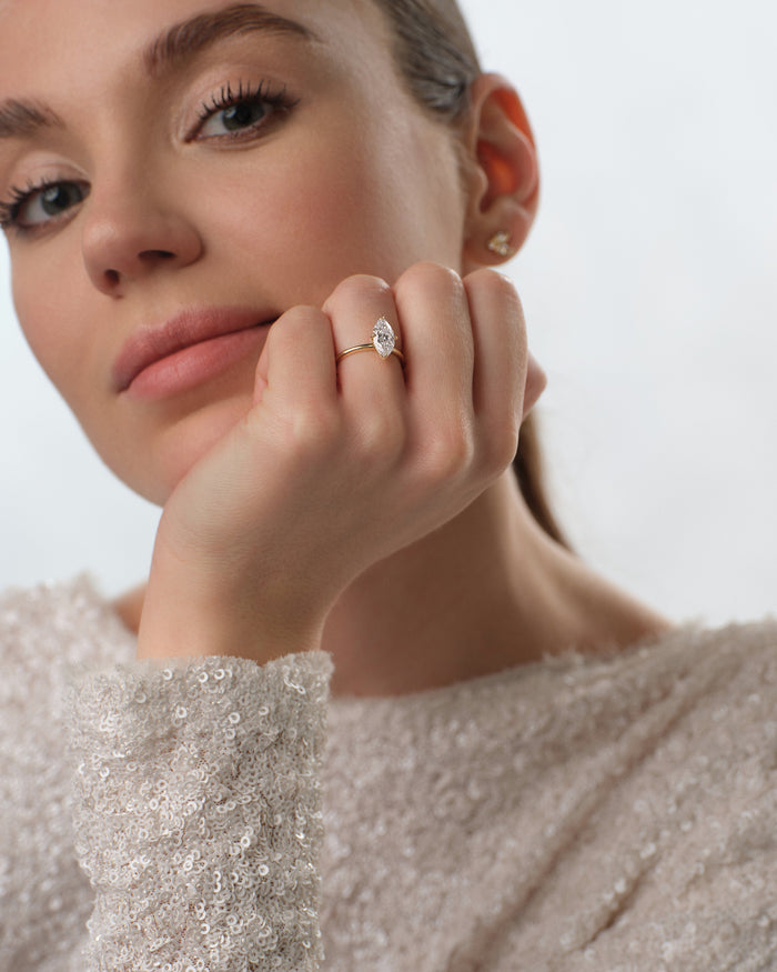 Marquise cut lab grown diamond ring in yellow gold worn with the hand at the chin, sequin sleeve