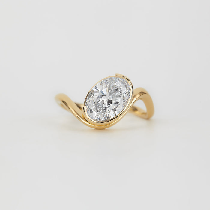 Oval cut moissanite angled half bezel engagement ring on a curved yellow gold band