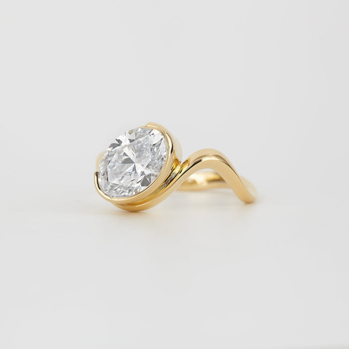 Oval cut moissanite angled half bezel engagement ring on a curved yellow gold band, view 2