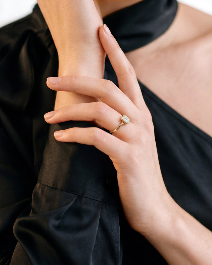 Oval moissanite bezel engagement ring in yellow gold worn on the hand against black fabric