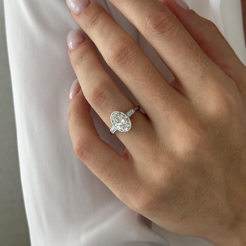 Oval moissanite bezel three stone engagement ring with tapered baguettes in white gold