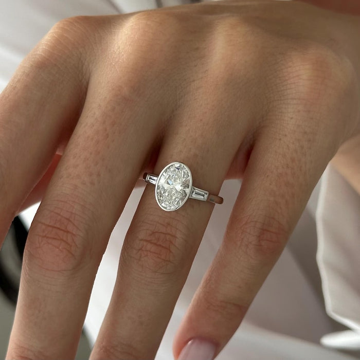 Oval moissanite bezel three stone engagement ring with tapered baguettes in white gold, view 2