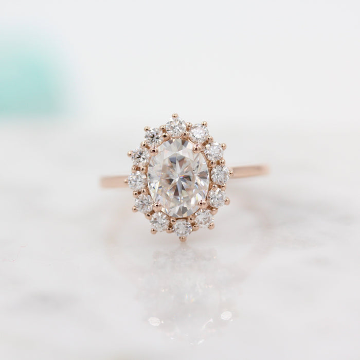 Oval cut moissanite claw set cluster halo engagement ring on a plain rose gold band
