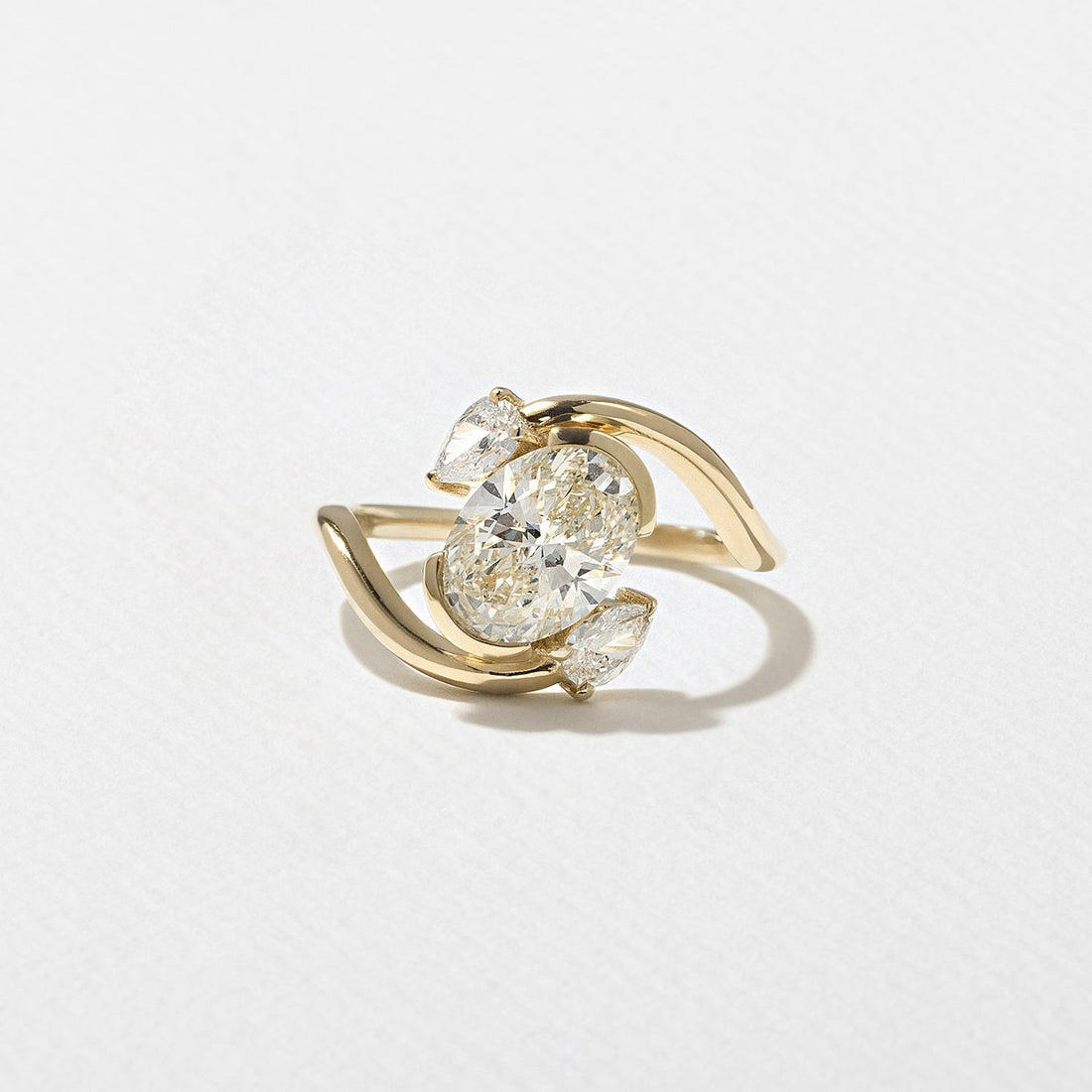 Oval cut moissanite diagonal swirl three stone engagement ring with pear accents in yellow gold