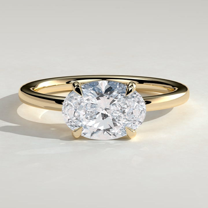 East west oval moissanite four claw solitaire engagement ring on a plain yellow gold band