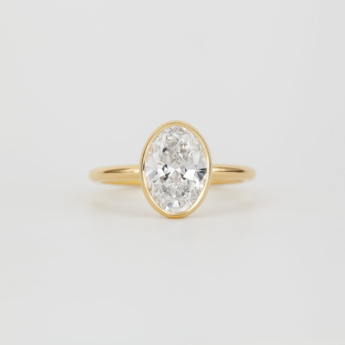 Oval cut moissanite full bezel solitaire engagement ring on a fine yellow gold band