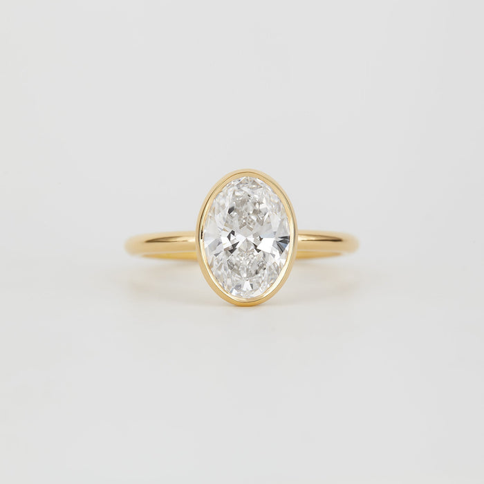 Oval cut moissanite full bezel solitaire engagement ring on a fine yellow gold band