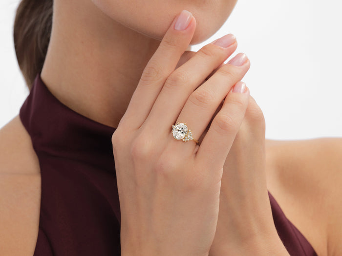 Oval moissanite floral cluster engagement ring in yellow gold worn on the hand