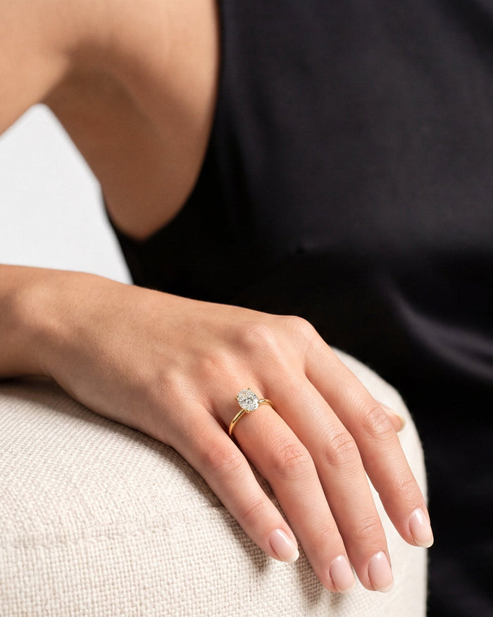 Oval moissanite hidden halo ring with plain yellow gold band worn on the hand resting on a chair