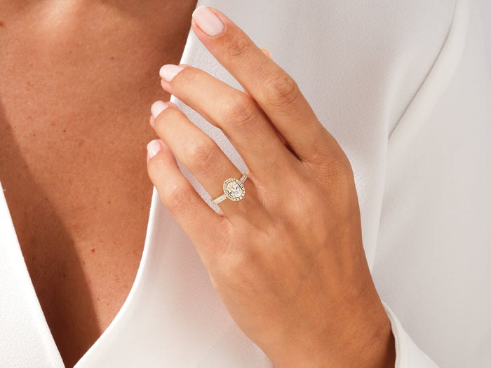 Oval halo moissanite ring with double pave shank on the hand, resting at the collarbone