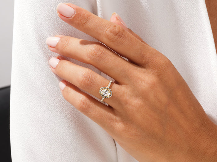 Dainty oval moissanite halo engagement ring in yellow gold worn on the hand