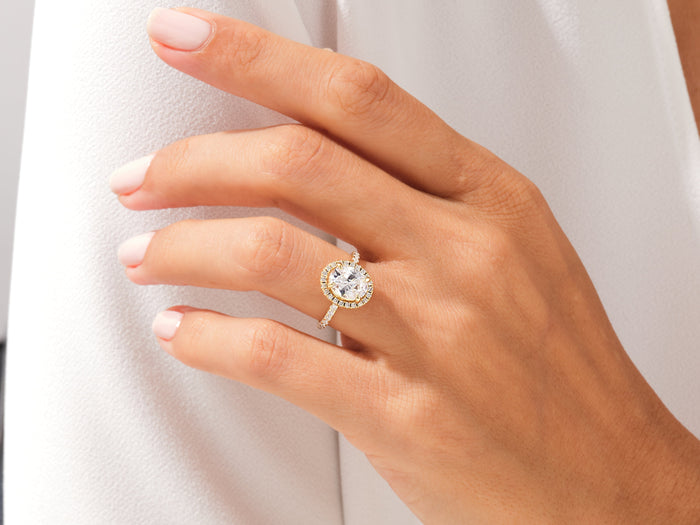 Oval lab grown diamond halo ring in rose gold worn on the hand against a white shirt