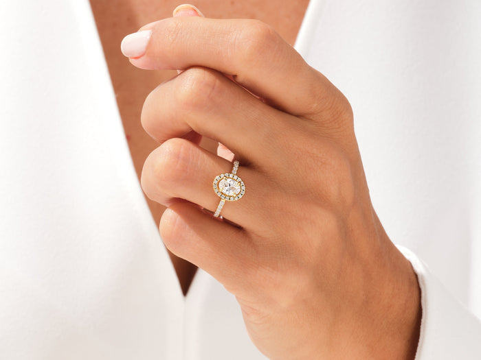 Oval lab grown diamond pave halo ring in rose gold worn on a hand held at the chest