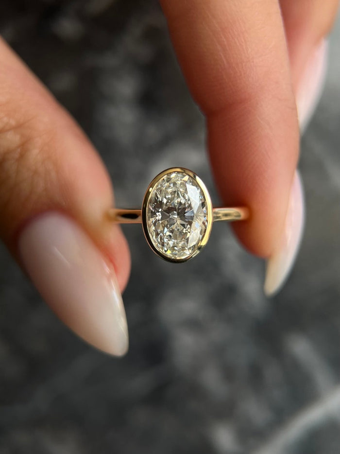 Oval cut moissanite heavy rim bezel solitaire engagement ring on a fine yellow gold band