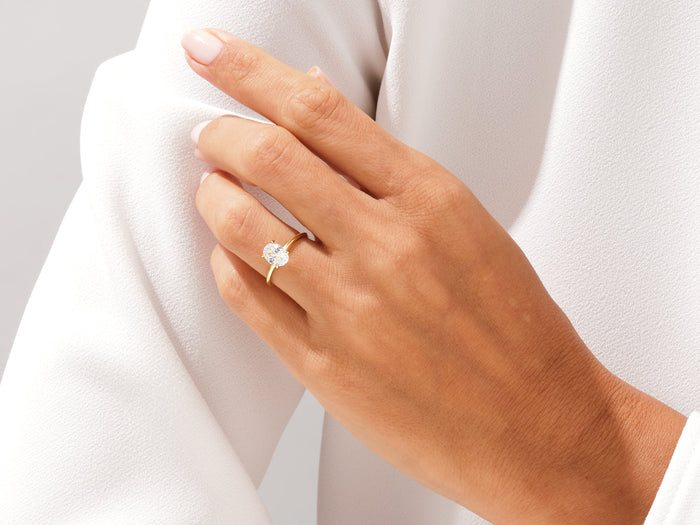Oval lab grown diamond four prong ring on a hand holding the edge of a white jacket