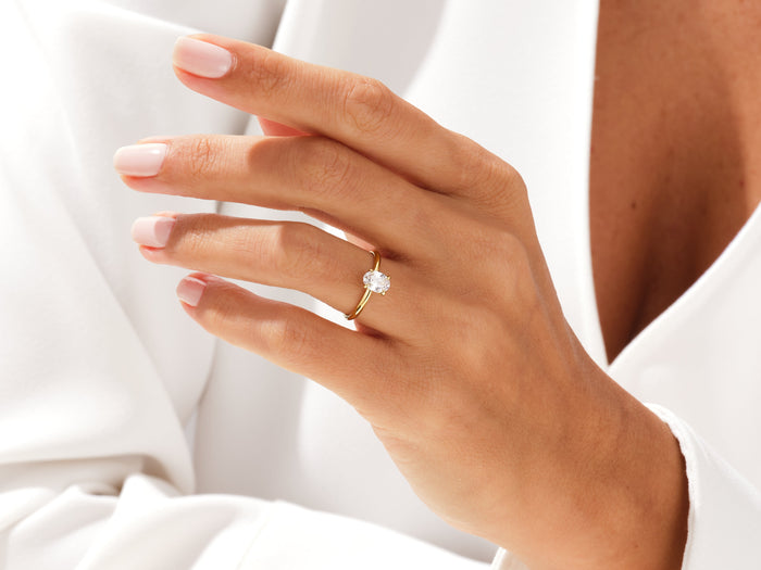 Oval lab grown diamond delicate solitaire on a hand raised near the neckline