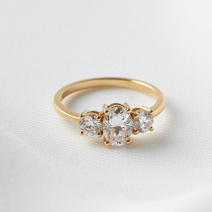 Oval cut moissanite three stone engagement ring with large round side stones on a flat yellow gold band