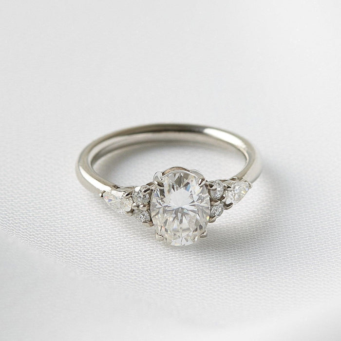 Oval cut moissanite with a pear and two rounds clustered at each shoulder in white gold