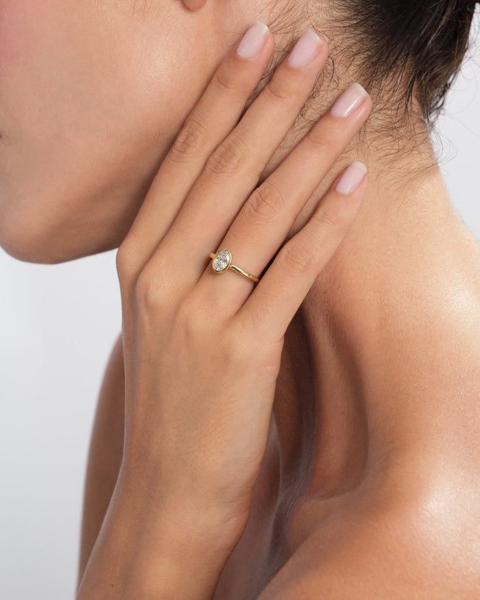 Oval lab grown diamond rub over bezel ring in yellow gold worn on the hand resting on the neck