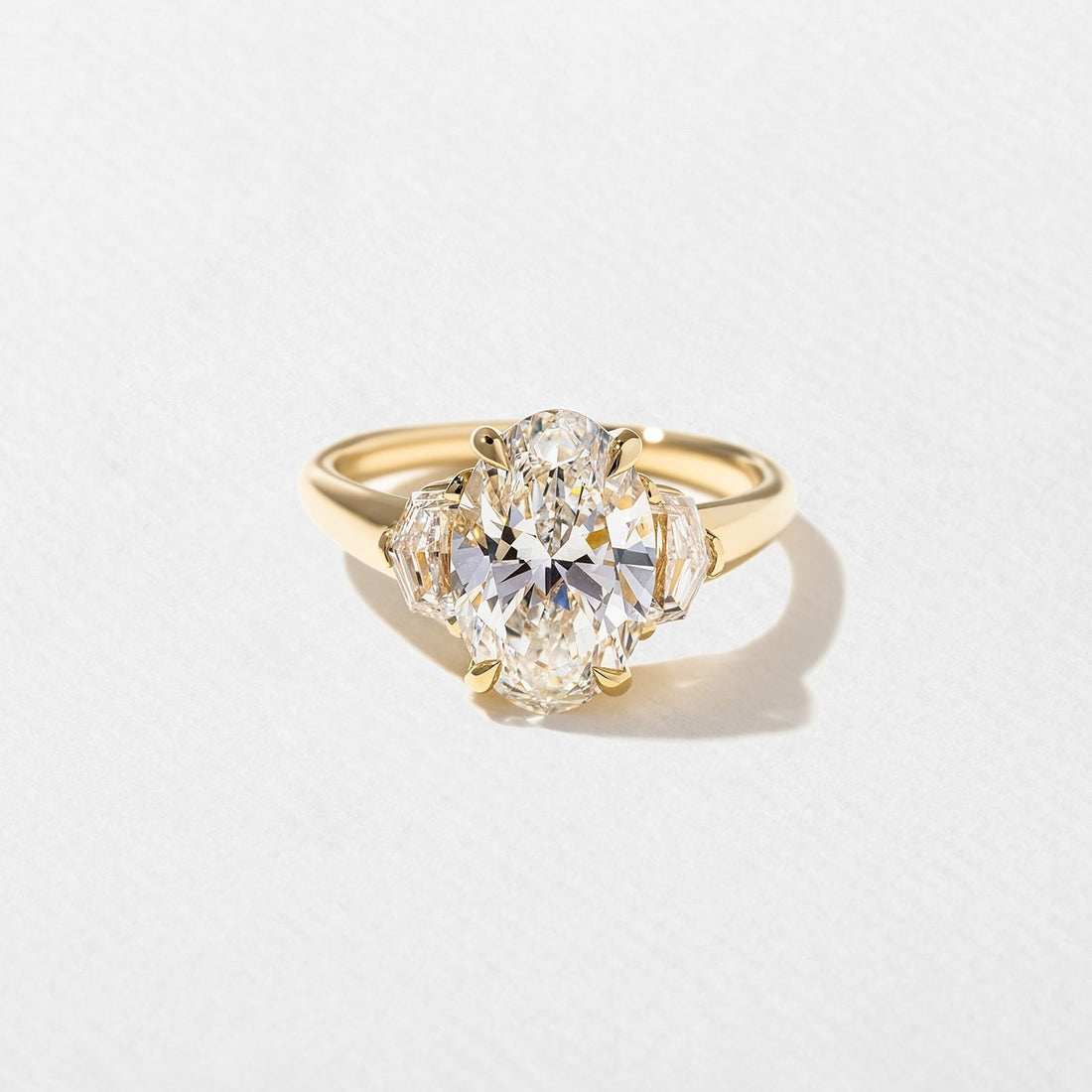 Oval cut moissanite three stone engagement ring with shield cut side stones in yellow gold