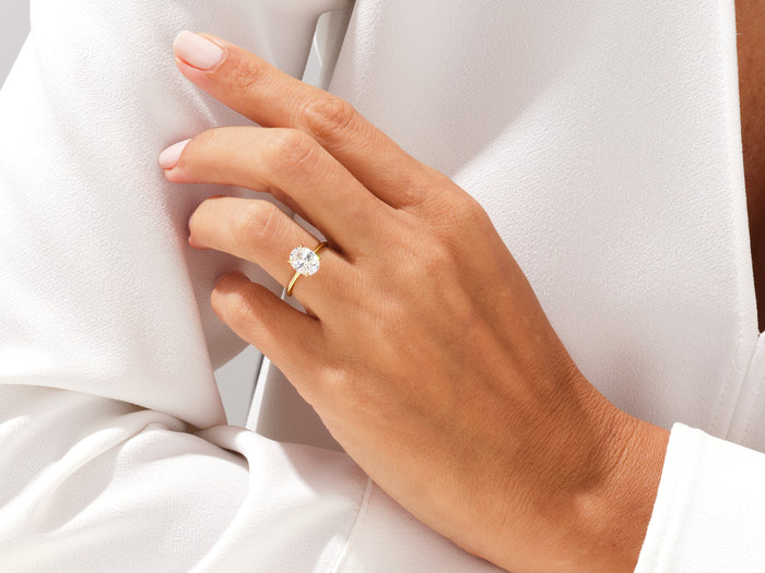 Oval cut moissanite four prong solitaire in yellow gold worn on the hand